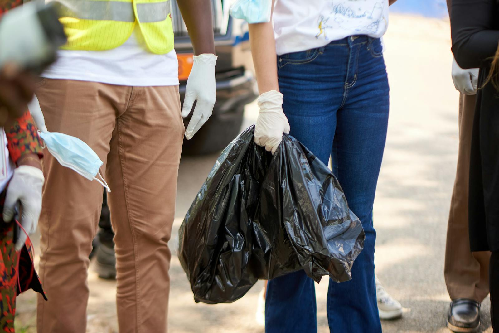 Volunteers participate in a street cleanup in Douala wearing gloves and carrying trash bags.